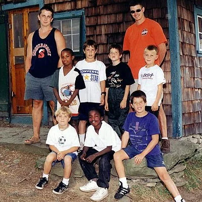 Campers and their camp counselors pose outside their cabin at summer camp.